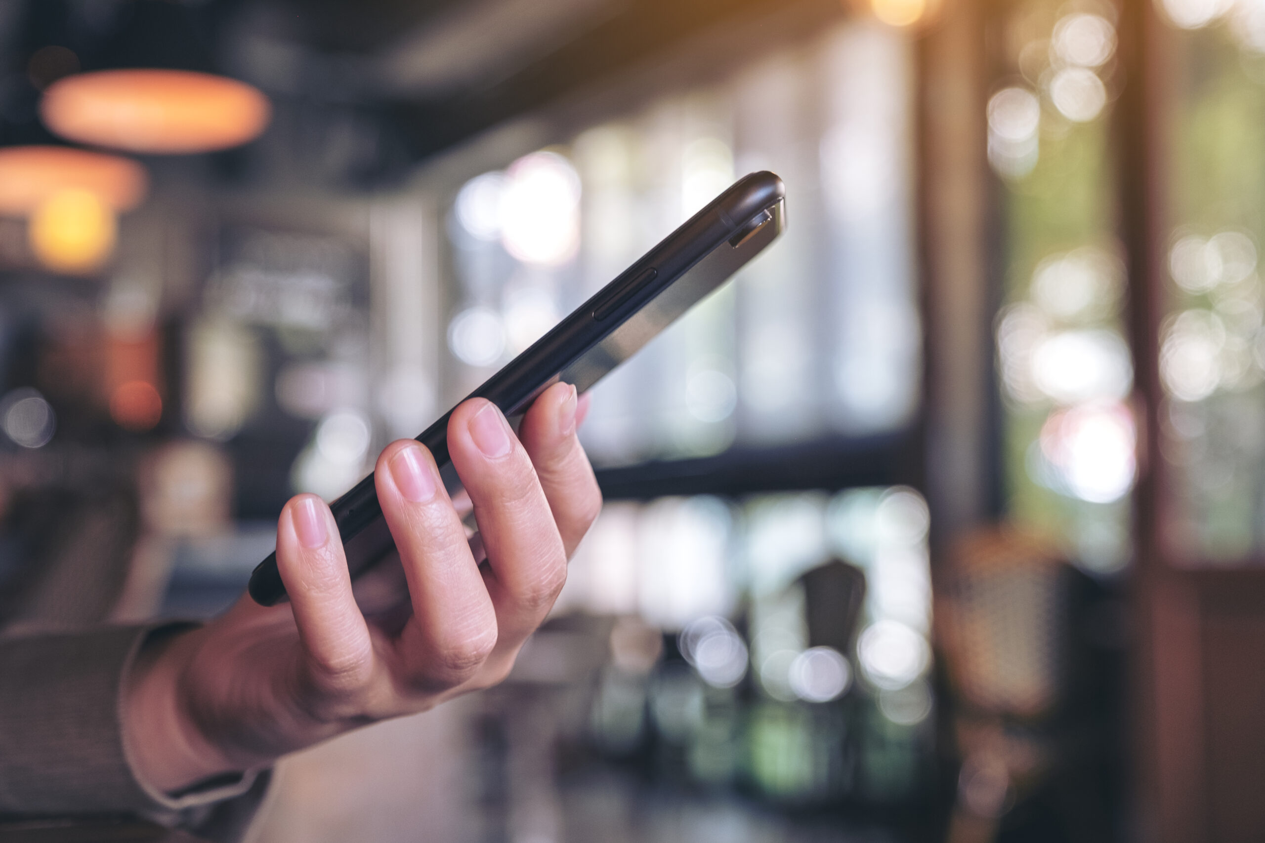 A woman holding and using a black smart phone with blur backgrou